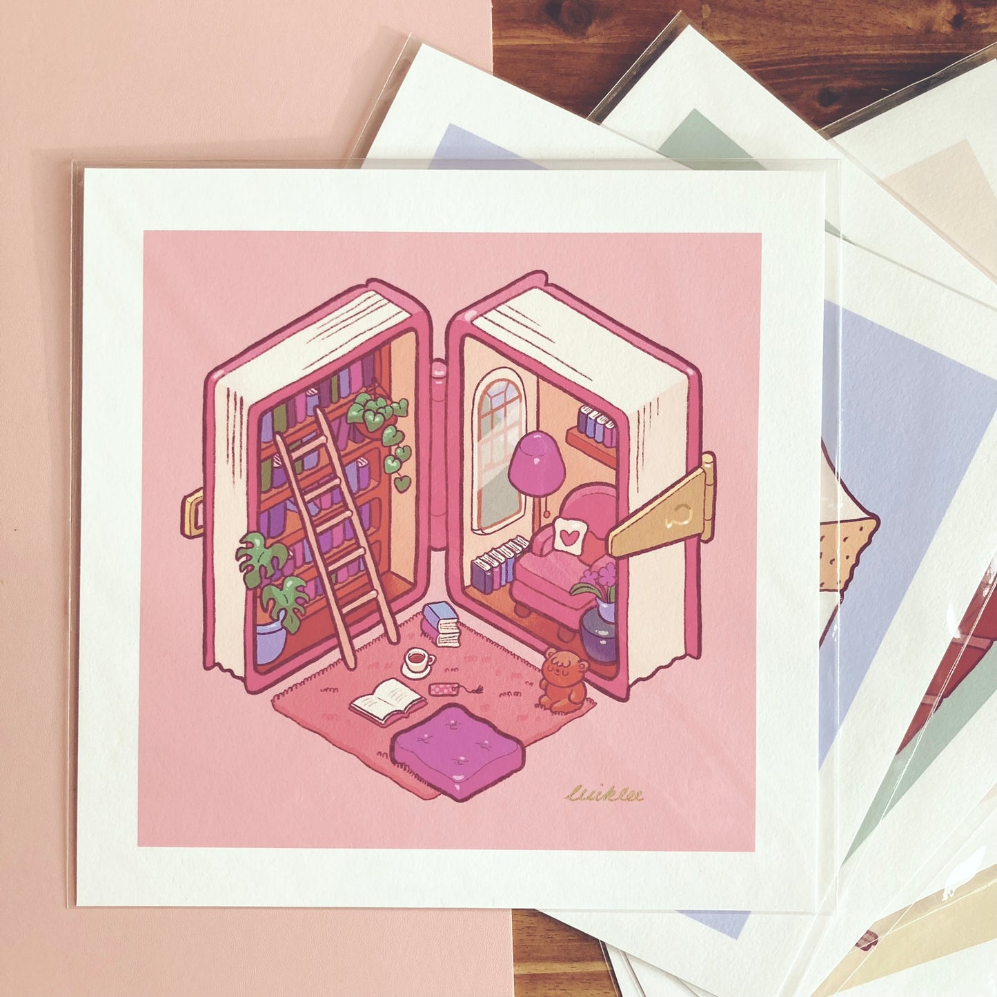 Kawaii-Illustration eines gemütlichen Miniatur-Zimmers in Form eines aufgeschlagenen Buches. Die linke Seite zeigt ein Bücherregal mit einer Leiter und Pflanzen, die rechte Seite eine kleine Sofaecke mit Lampe und Dekoration. Auf dem weichen Teppich liegen ein offenes Buch, eine Tasse Tee und ein Kissen. Das Farbschema ist sanftes Rosa mit warmen Akzenten. Perfekt für Bücherliebhaber und Fans von gemütlicher Kunst!